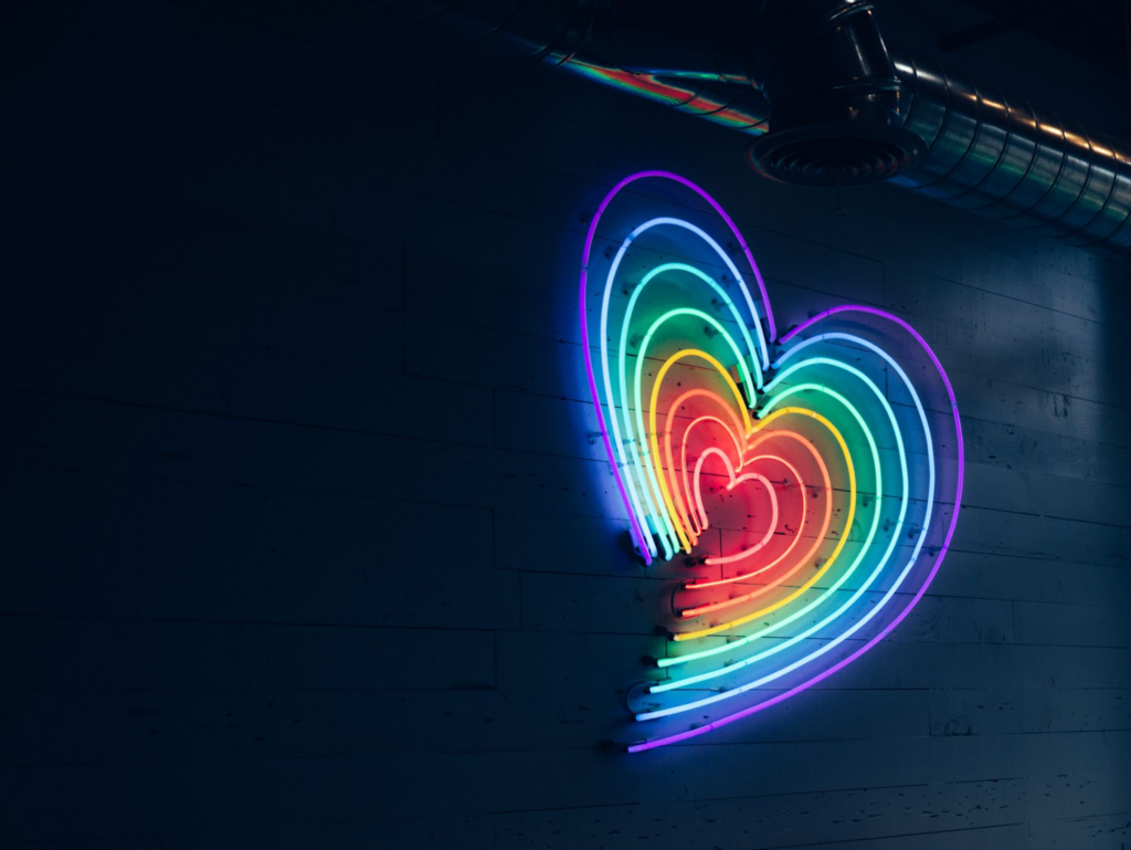 A series of concentric neon hearts arranged from red in the center to purple on a black brick wall.