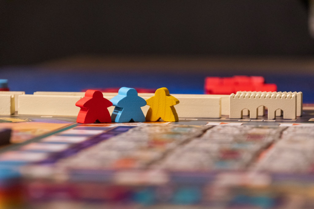 A red, blue, and yellow meeple in front of some other wooden pieces on a game board.