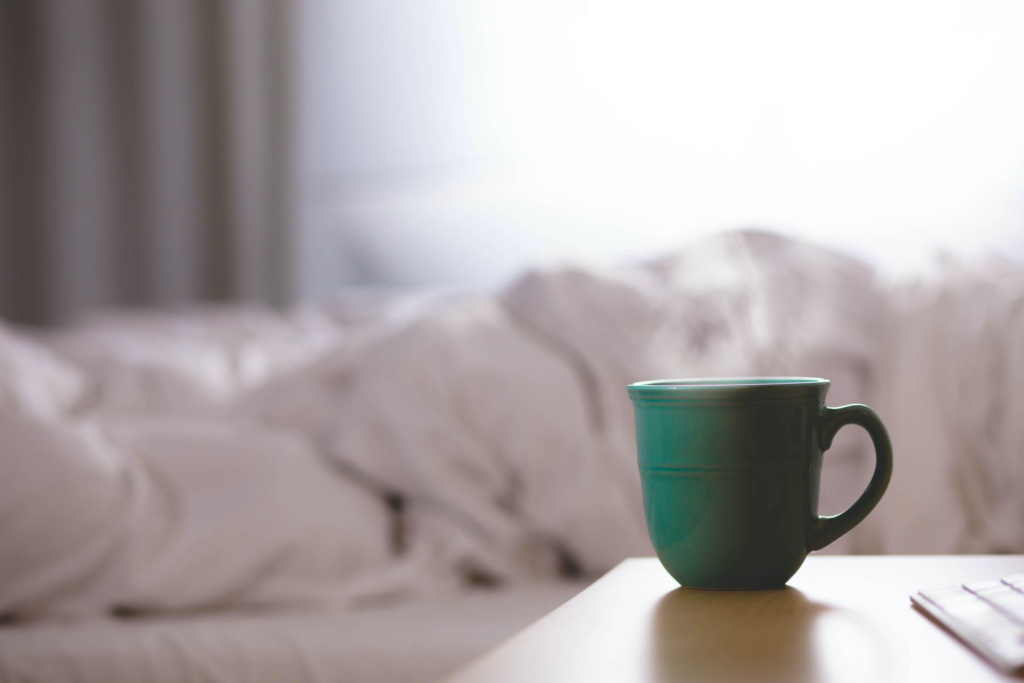A turquoise/green cup on the edge of a nightstand next to a body asleep under a comforter.