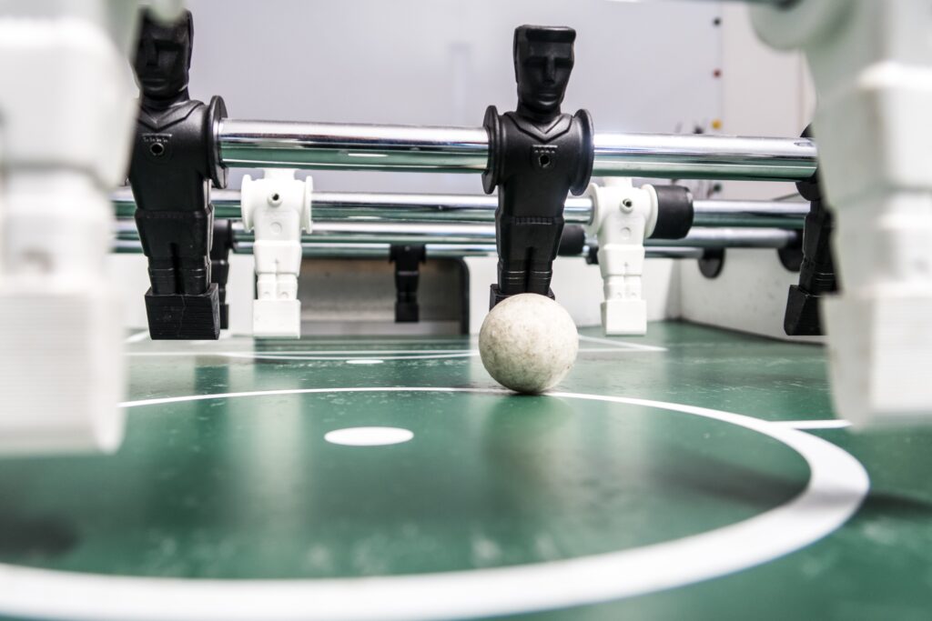 Black and white foosball players on a green table. The ball is poised for the first kick off.